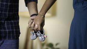 couple holding hands with baby shoes