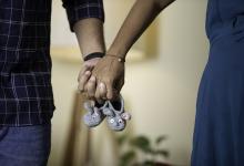 couple holding hands with baby shoes